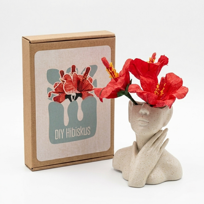 DIY Bastelset Hibiskus aus Krepppapier mit drei roten Blüten in einer Keramikvase neben der Verpackung von Woodwormis World