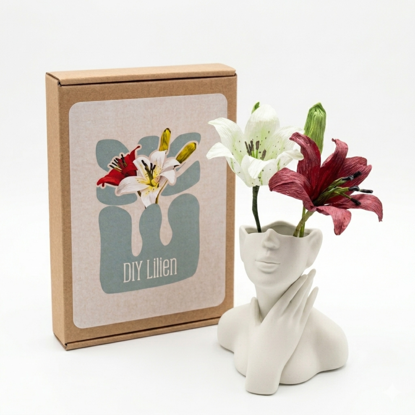 DIY Bastelset Lilien aus Krepppapier mit drei zwei Blüten in einer Keramikvase neben der Verpackung von Woodwormis World